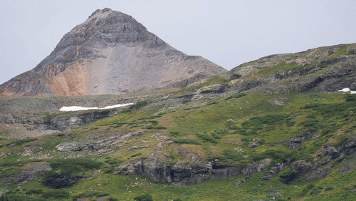 image of a hilly region featuring a huge mountain in the background with vast stretches of lush green grasslands 