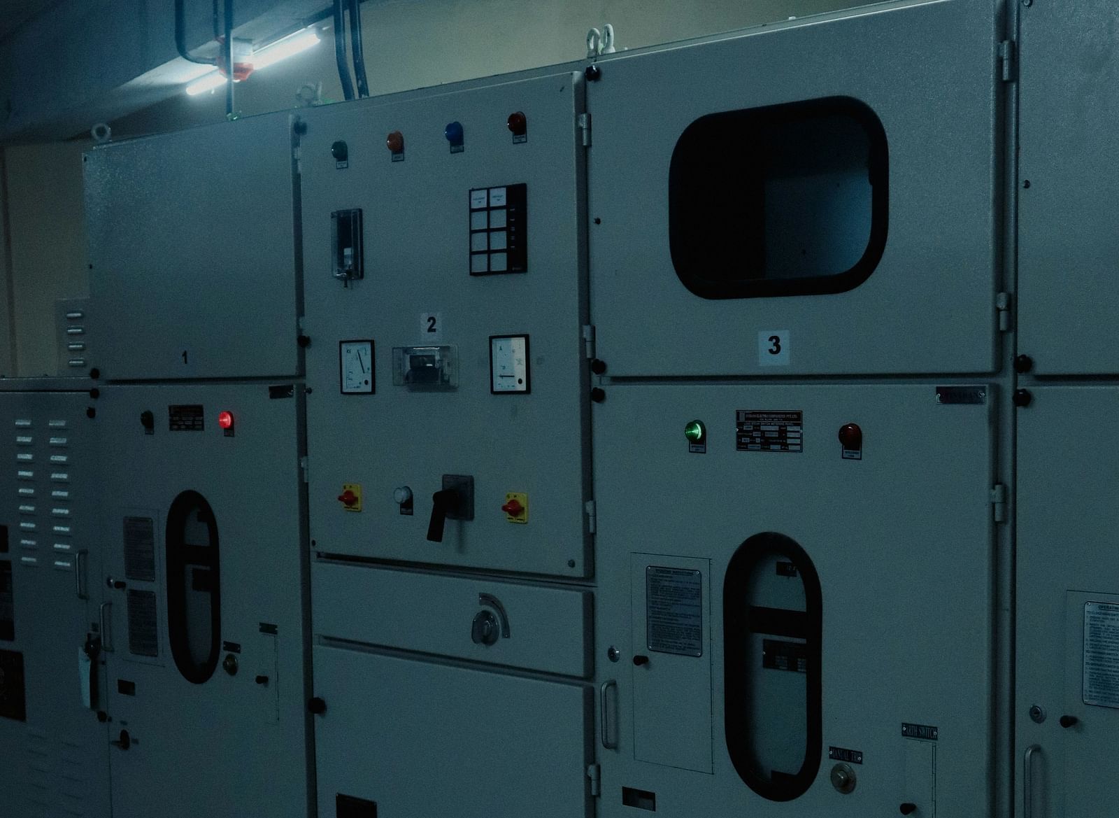 A row of industrial grey electrical panels with various gauges, switches, and indicator lights.