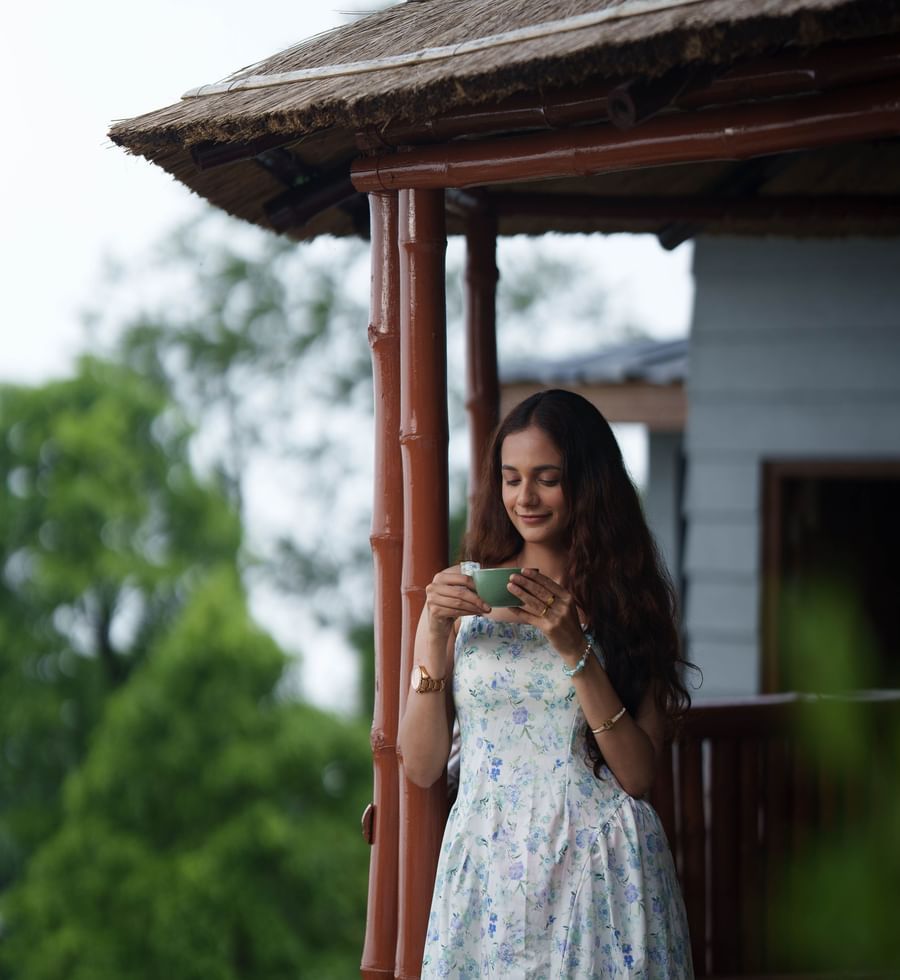 A woman in a white dress stands outside a small wooden gazebo or structure, looking out, at Summit Enigma Resort and Spa.