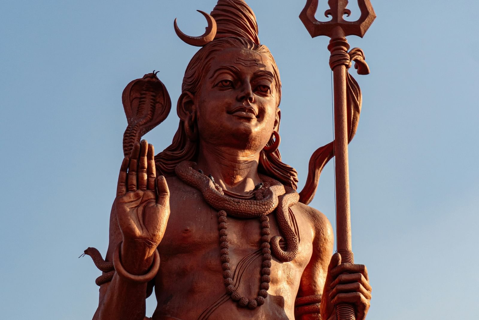 A bronze statue of the Hindu god Shiva, under a blue sky.