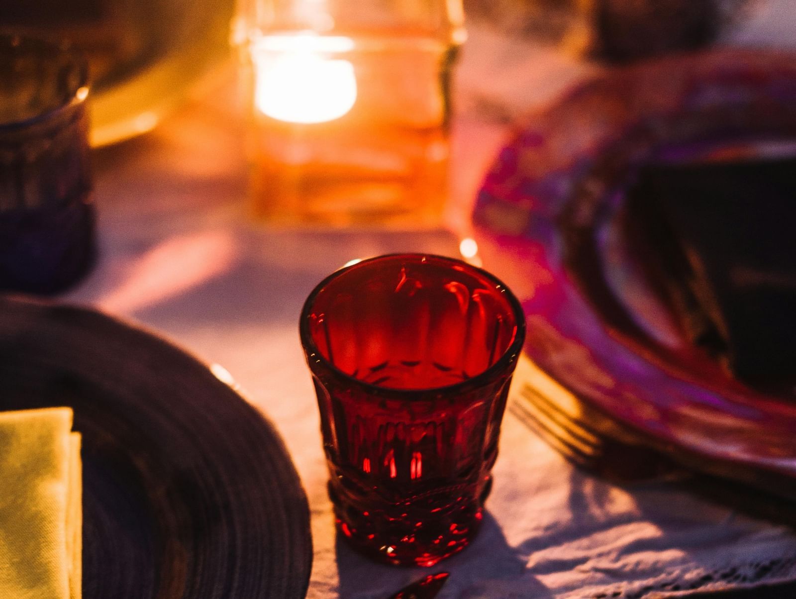 Elegant candle-lit dinner setup with a red glass and cutlery on a table.