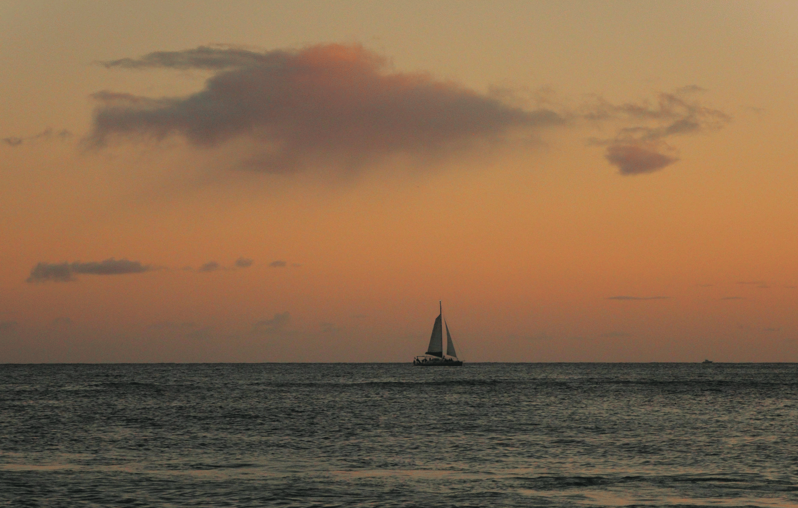 Distant sailboat on a calm sea during sunset, with a golden-pink sky and rippling water.