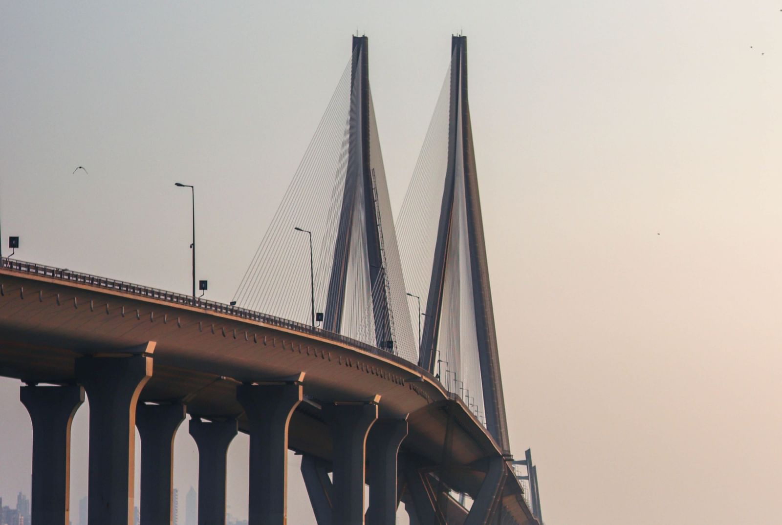 A view below of a bridge in mumbai city on the sea with rocks in the forefront.