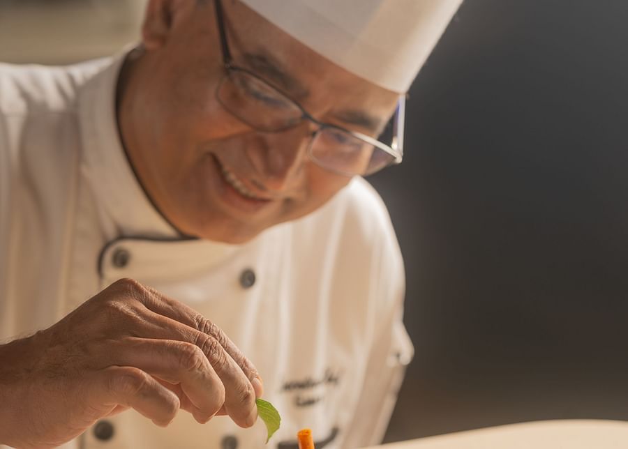 A close-up of a happy chef garnishing a meal on a plate at The Ananta Udaipur, adding final touches with a smile.