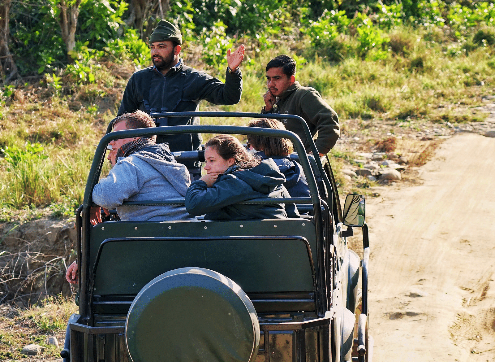 A safari jeep with passengers inside it looking towards the forest on a bright sunny day - Ivory Destinations