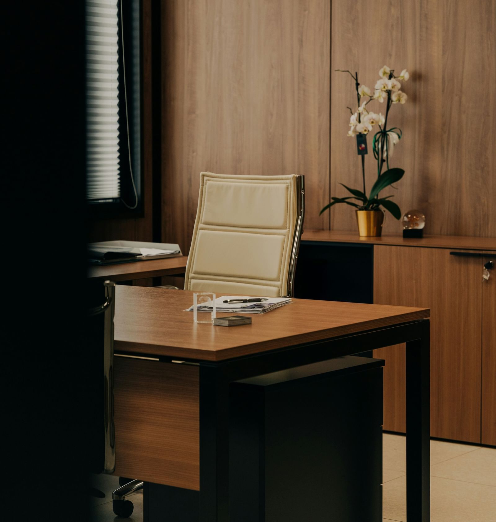 A neat office with a wooden desk, a beige chair, and an orchid plant adding elegance to the space.
