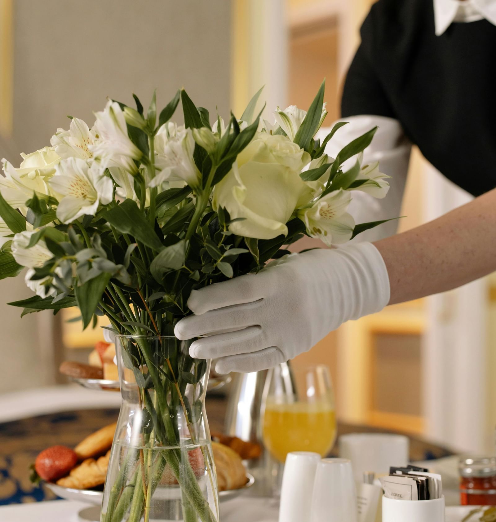 Hotel staff arranging flowers in a vase with tea service tray reflecting warm hospitality.
