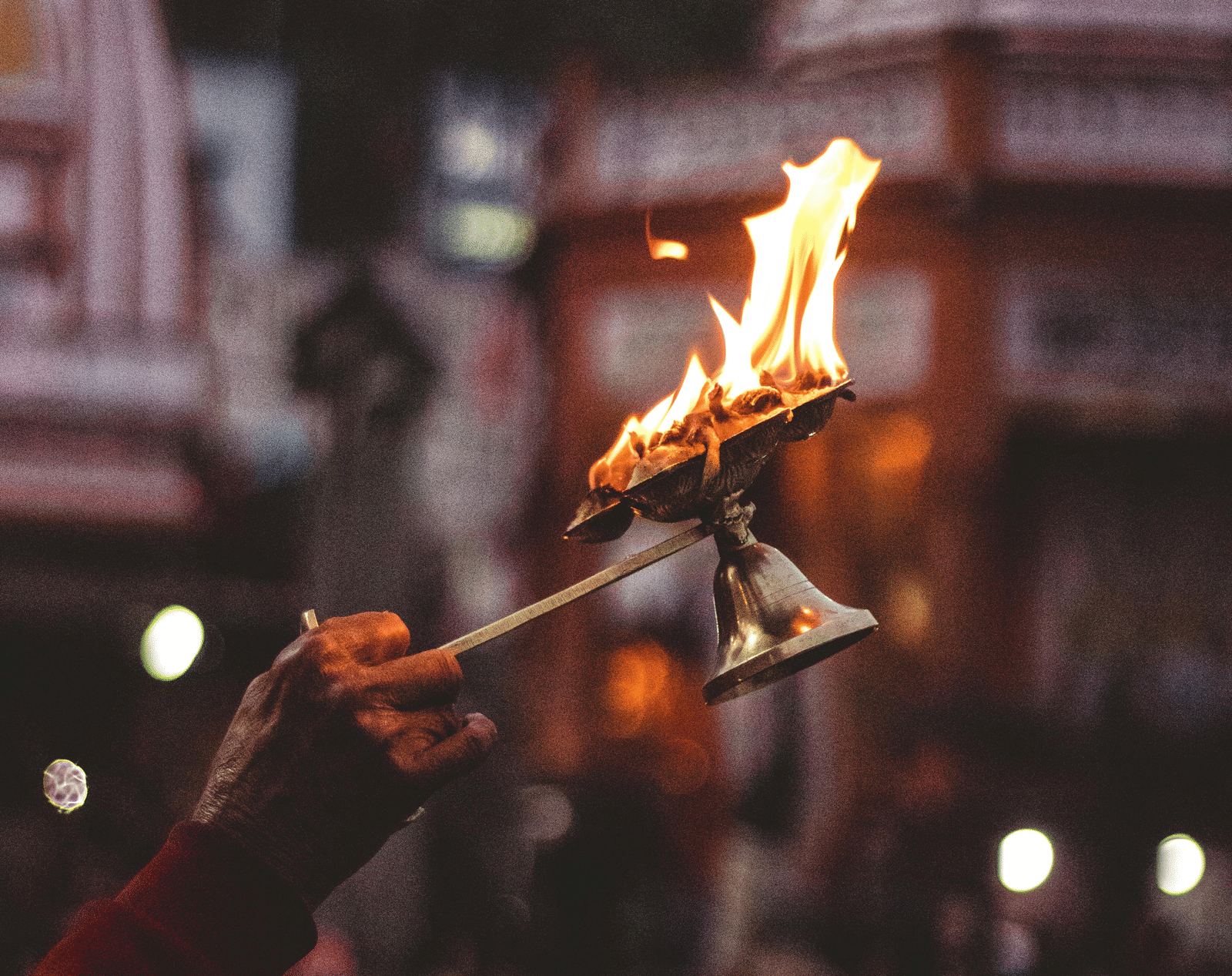 A close-up shot of a person holding a lit torch with flames, with a blurred crowd in the background.