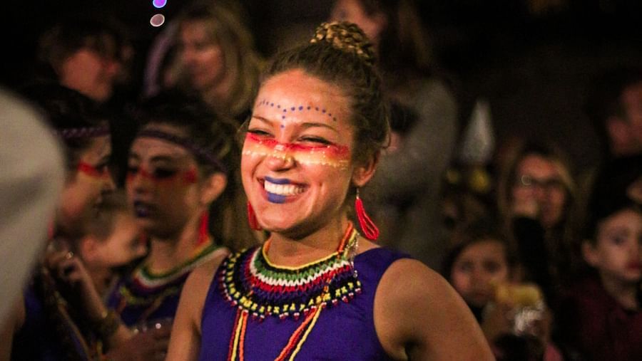 a woman captured with a beautiful smile while she has her face painted for a carnival and is wearing vibrant red and blue clothes