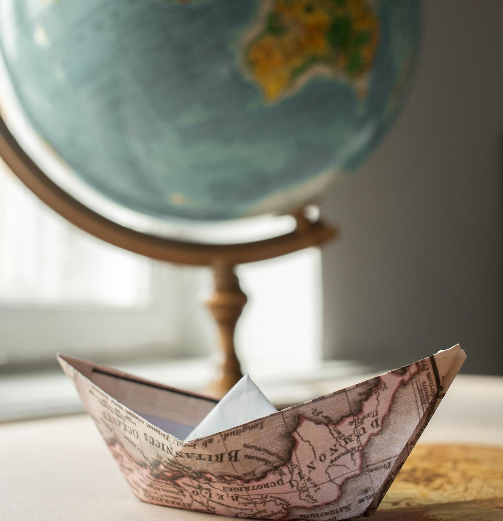 A paper boat made from a map, with a globe in the background