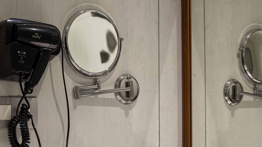 Image of the bathroom in Coral Premium Room at Coral Reef Hotel and Spa in Port Blair featuring a sink and a large mirror over it along with a hair dryer and mini shaving mirror next to it