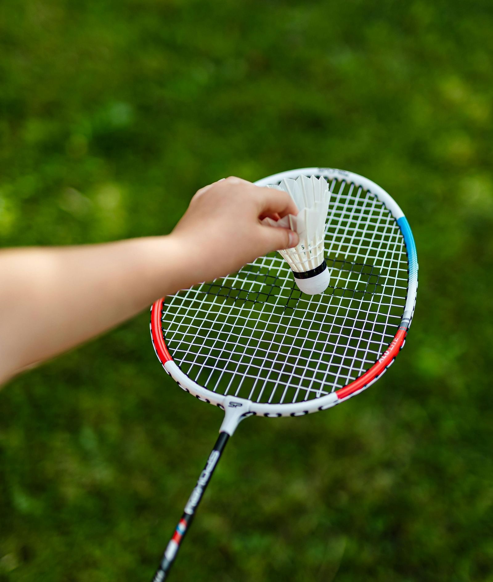 A hand holding a badminton racket and shuttlecock, poised and ready to serve