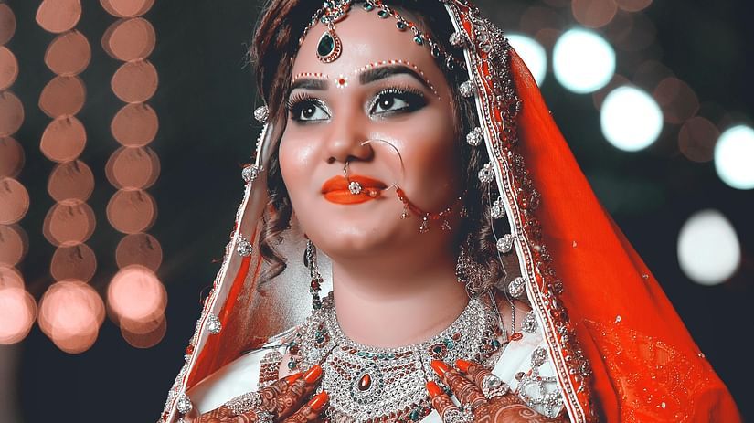 A bride adorned with jewelry wearing a red-white saree with a red dupatta on her head