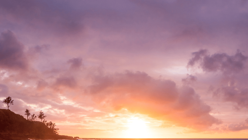The shore of a beach during sunset, with waves reflecting the warm colours of the sky.
