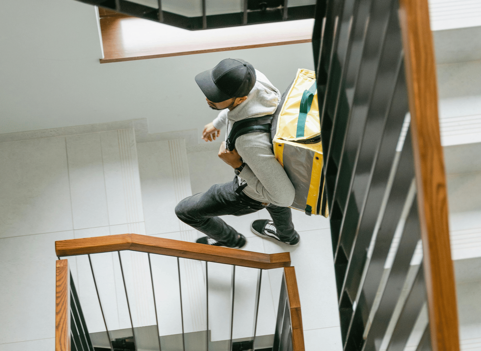 A person wearing a delivery bag on his back, climbing up the stairs.