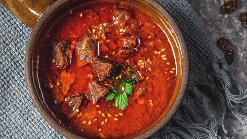 image featuring a bowl of Red meat curry topped with coriander leaves