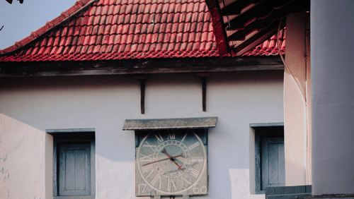A vintage clock hanging on the wall outside a traditionally built Kerala building.