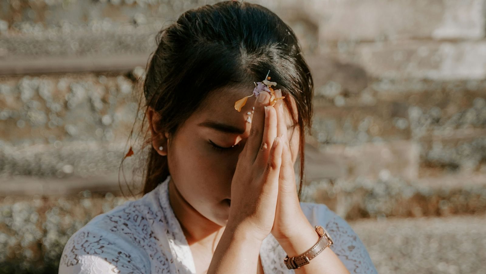 a woman praying with hands folded against her head with a wall in the background
