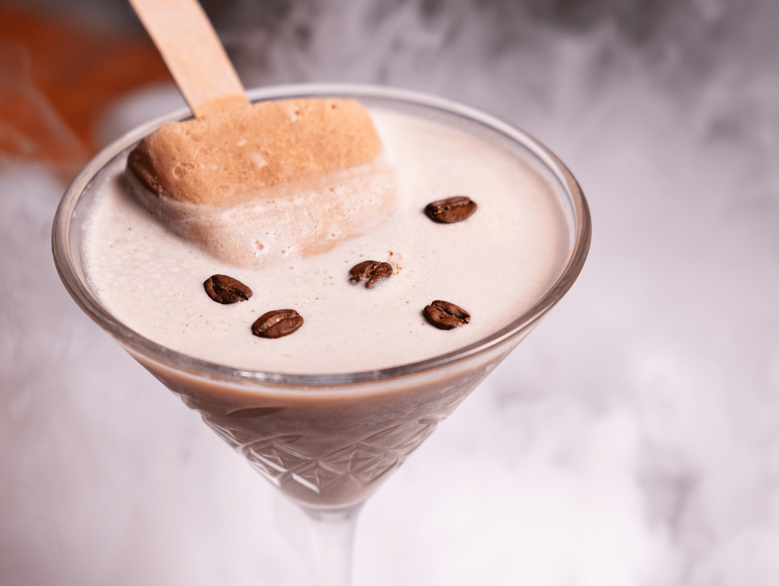 A creamy espresso martini topped with coffee beans and a popsicle stick, surrounded by a misty cloud effect for a dramatic presentation at Papaya Tree Hotels.