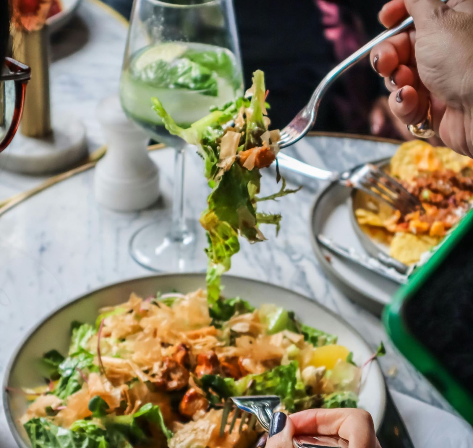 2 people dining together sharing a wholesome salad with a wine glass kept besides the plate.