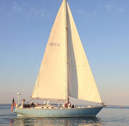 White sailboat gliding on calm waters at sunset near Hartstone Inn.