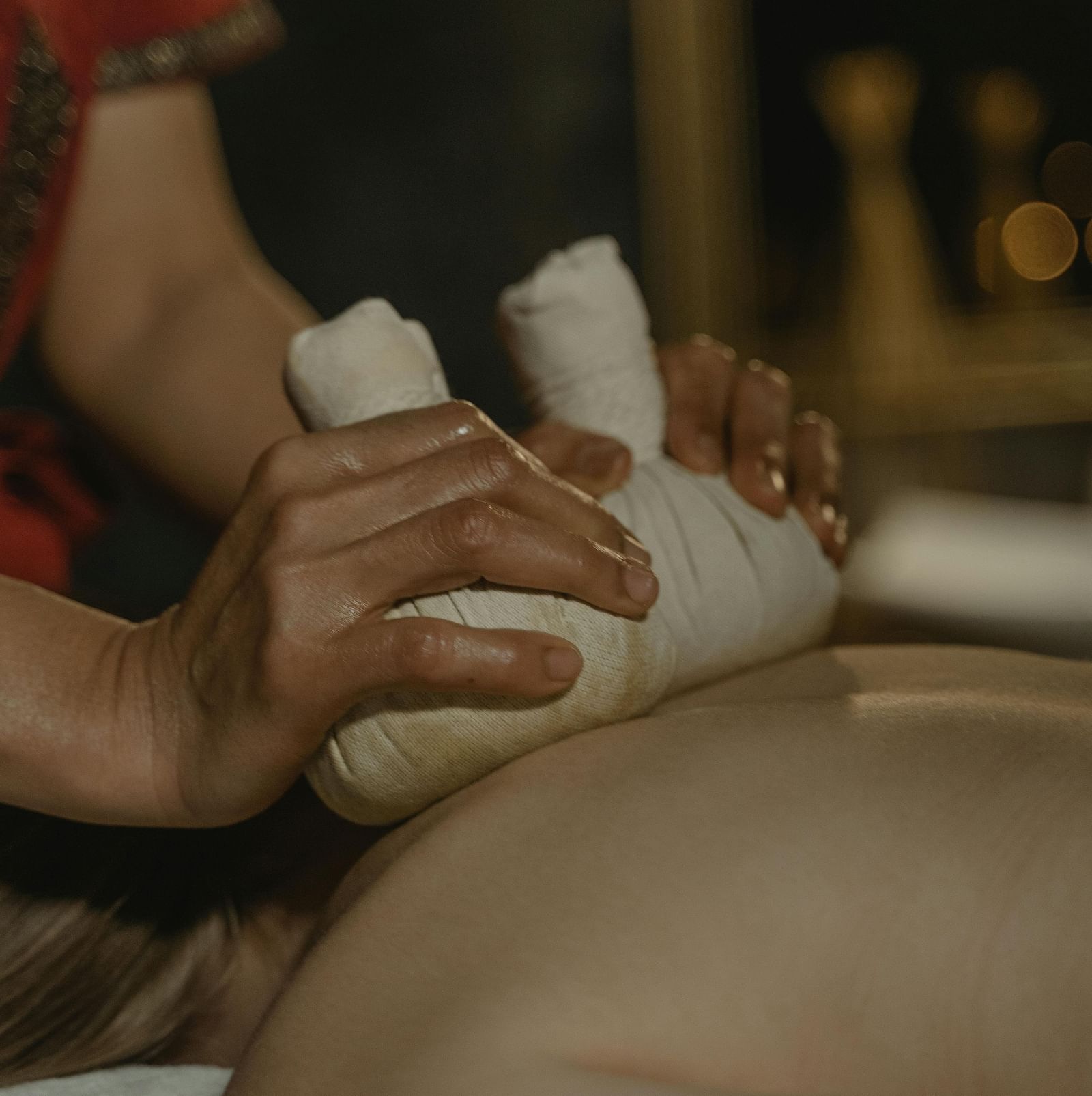 A masseuse using cloth bundles to press the back of a person.