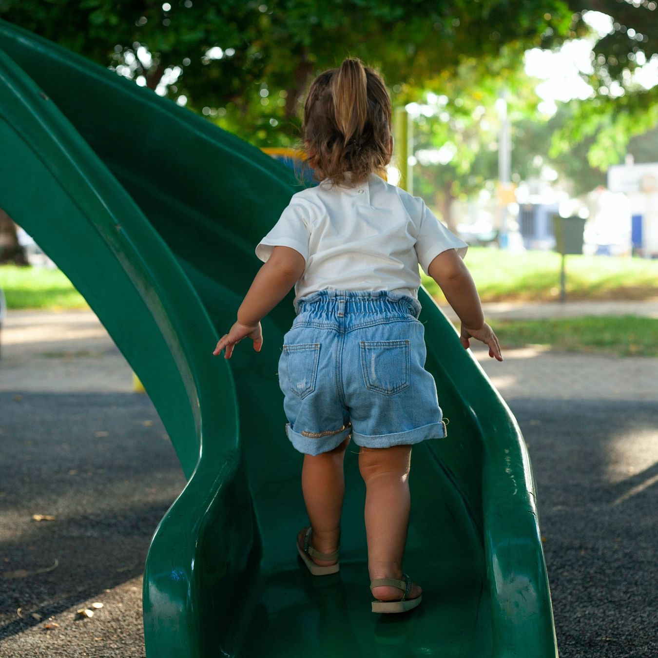 A kid walking up a green slide during the day