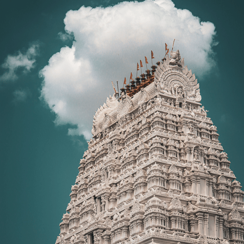 A view from below of the intricate art on the gopuram of the temple in Tirupati, with a cloud behind it.