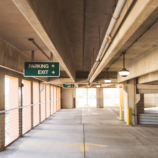 A brightly lit parking garage with signs pointing to the parking area and exits.