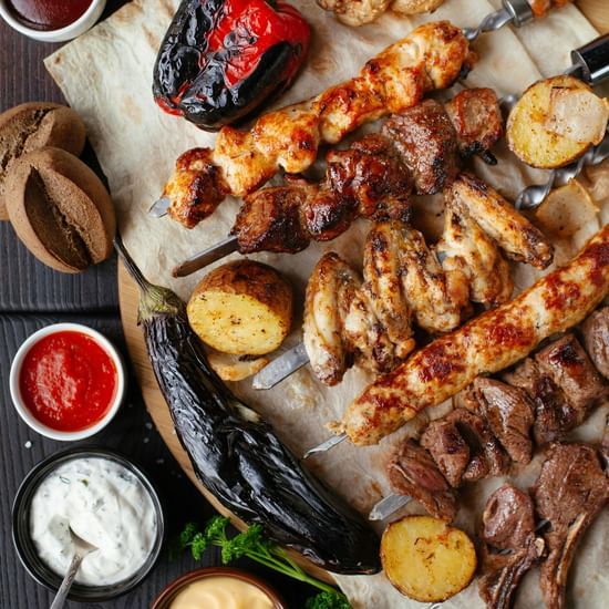 A delicious assortment of grilled meats, vegetables, and sauces laid out on a wooden table.