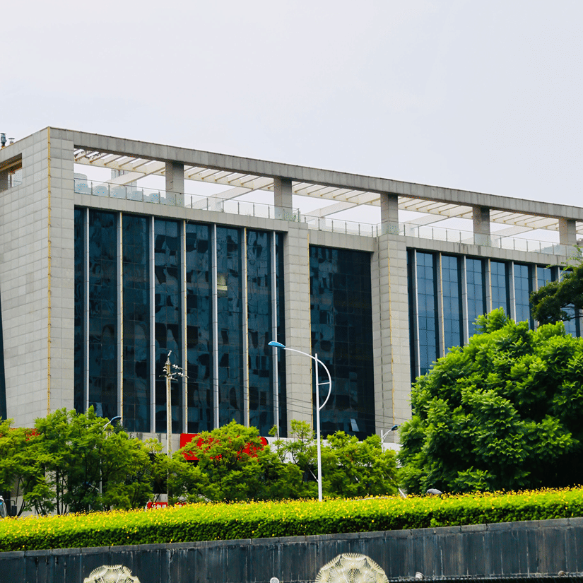 A sleek modern office building stands behind manicured green lawns and vibrant flowering plants under a bright sky.