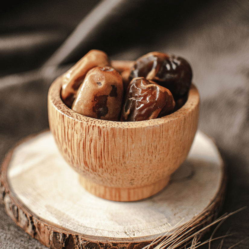 A view of a numerous dates kept in a small cup, placed on a wooden coaster with wheat straws next to it. Dates is one of the best things to buy from Qatar when travelling back to your home country.