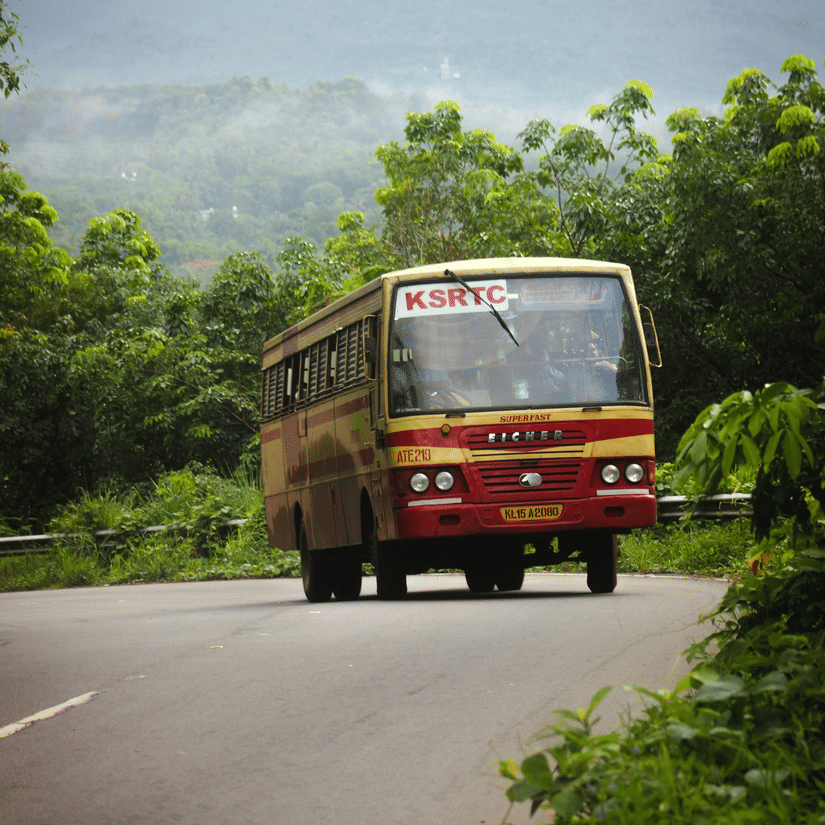 A red bus driving on a winding road through a hilly, forested area.