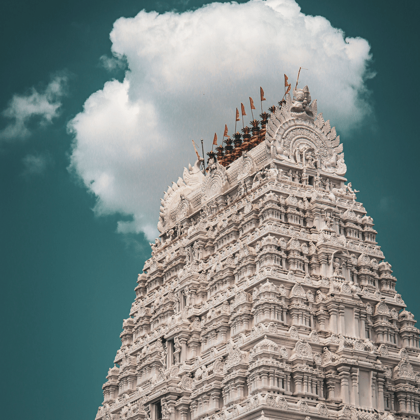 A view from below of the intricate art on the gopuram of the temple in Tirupati, with a cloud behind it.