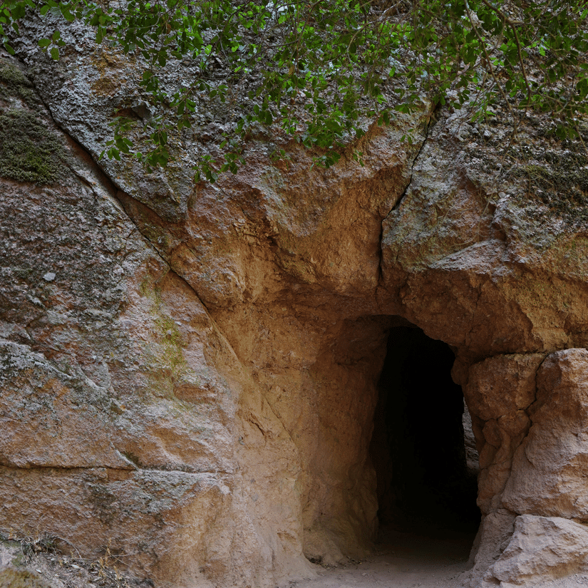 An overview of a cave entrance with a narrow opening and vegetation above the entrance at Sita Gufa, Nashik.