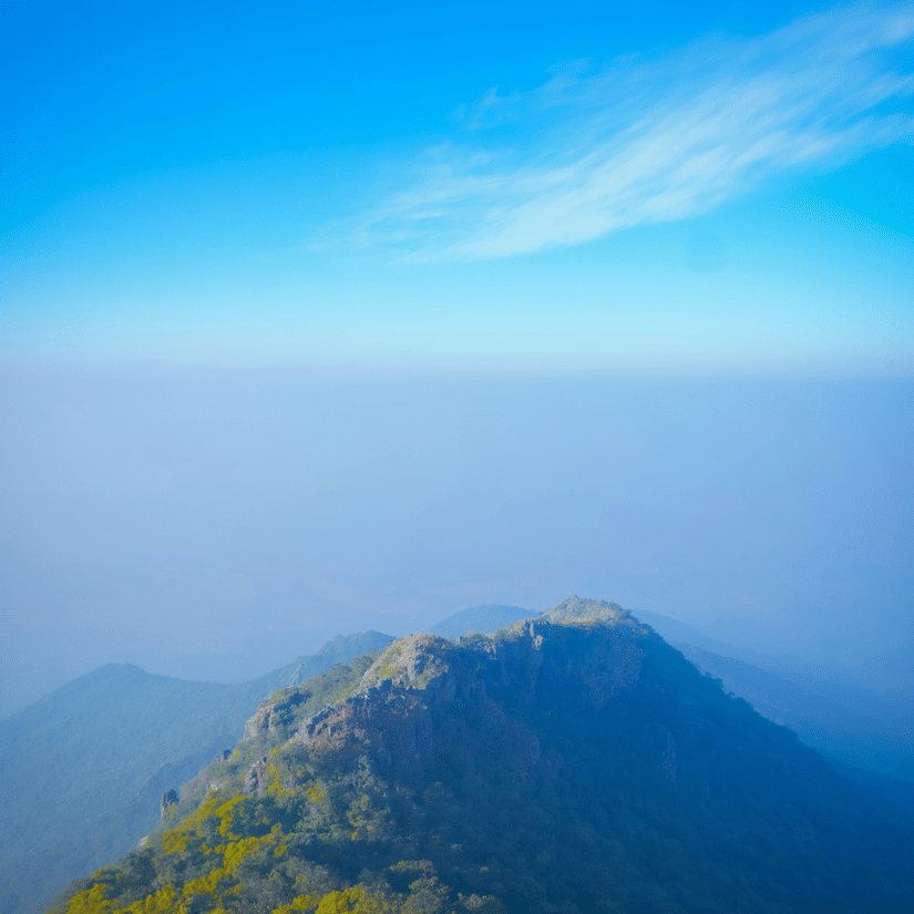 Panoramic view of a rugged mountain peak and lush green valleys seen from Parasnath Hill under a clear blue sky.