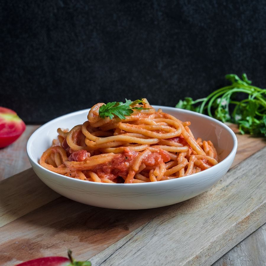 an image of a bowl containing red sauce spaghetti garnished with basil leaves kept on a wooden table