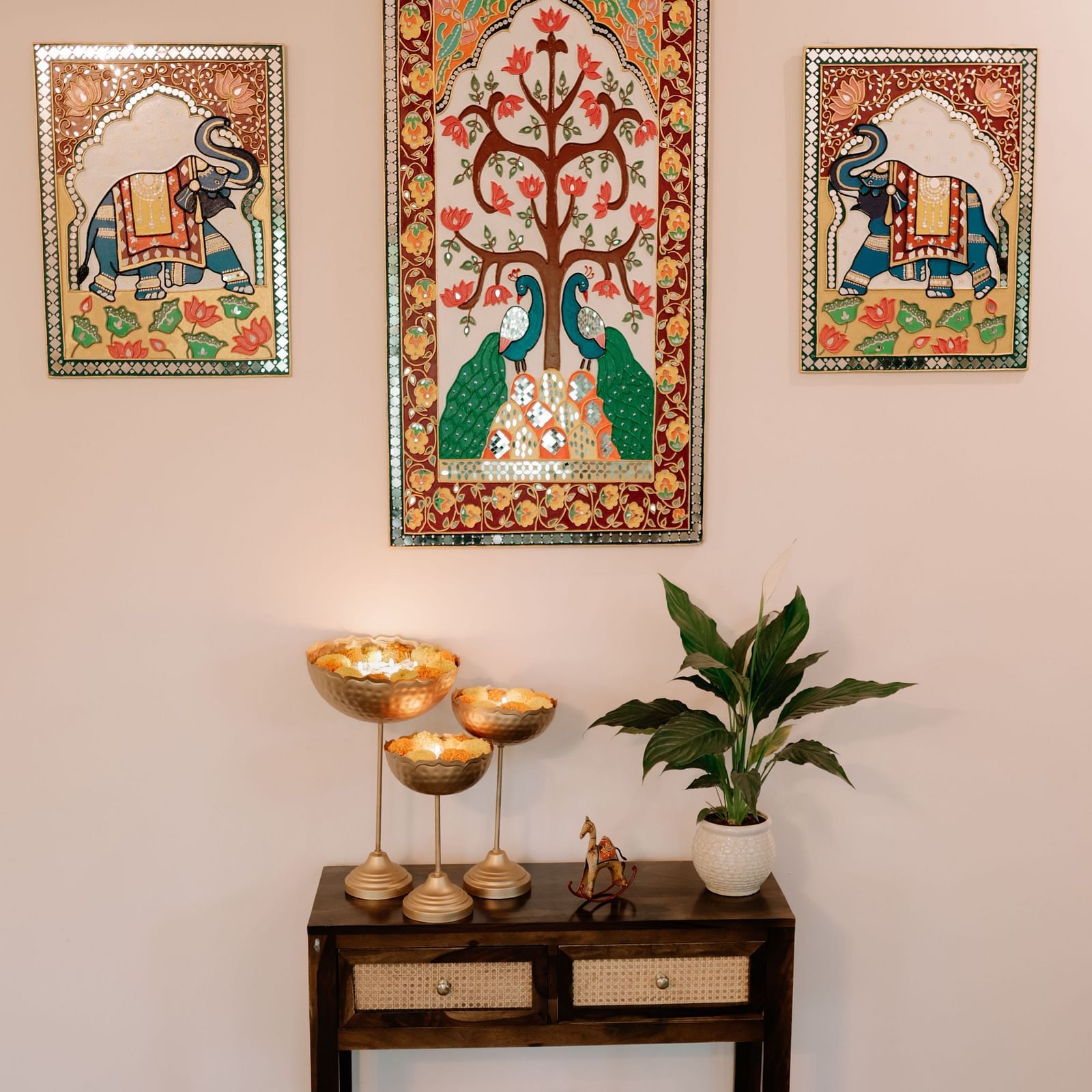 A small table with decorative bowls and a plant, beneath wall art featuring peacocks and a tree of life | Adhyaya Heritage Reverbed