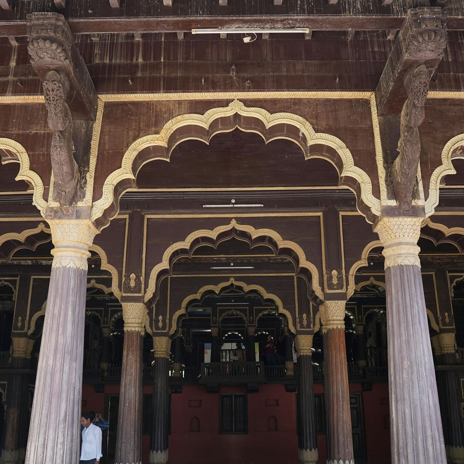 A grand entrance to a historical Indian palace, featuring ornately carved arches and wooden beams.
