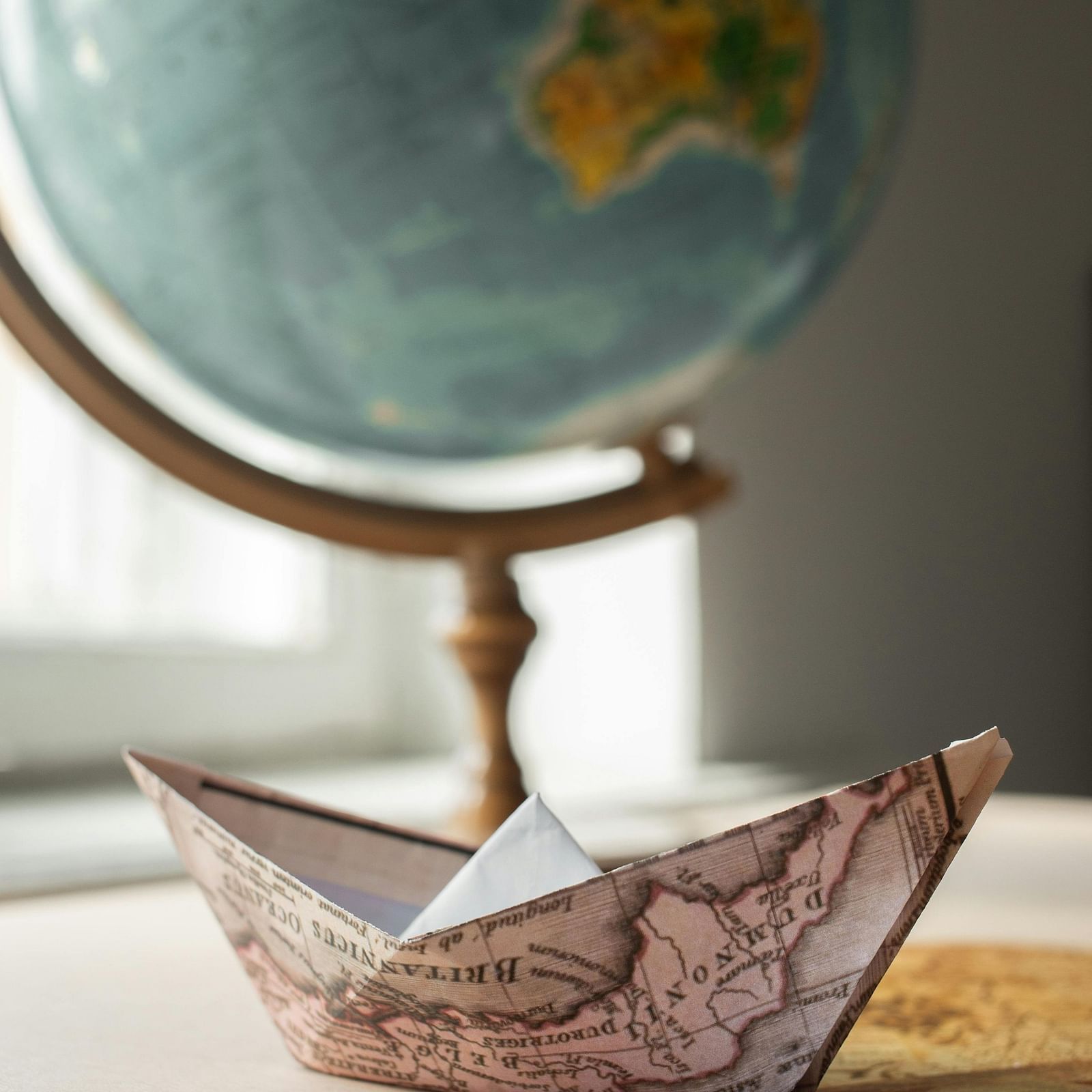 A paper boat made from a map, with a globe in the background