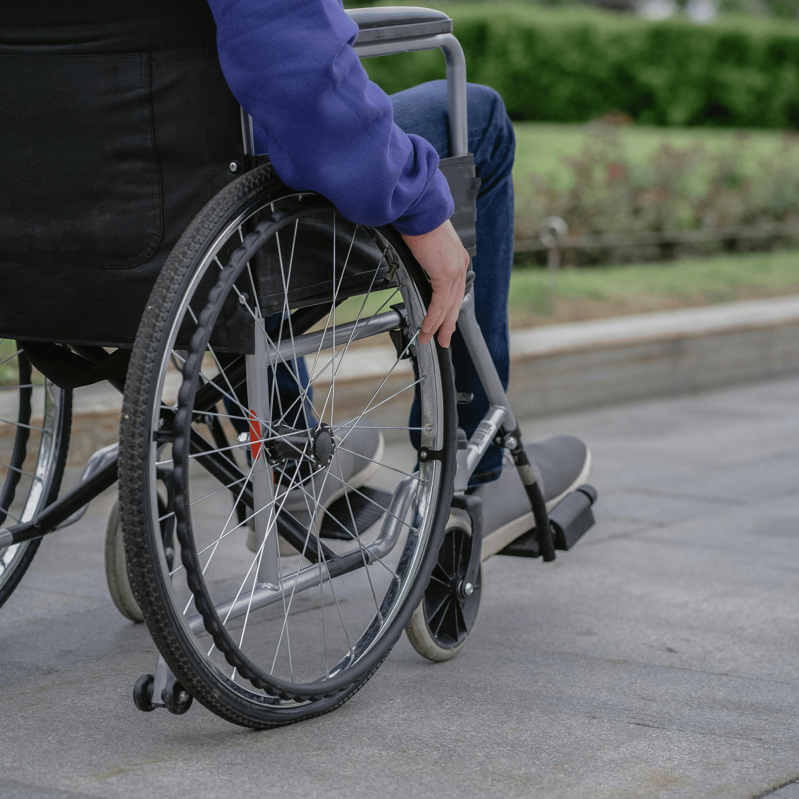 Close up shot of a person sitting on a wheelchair with his hand on the wheel.
