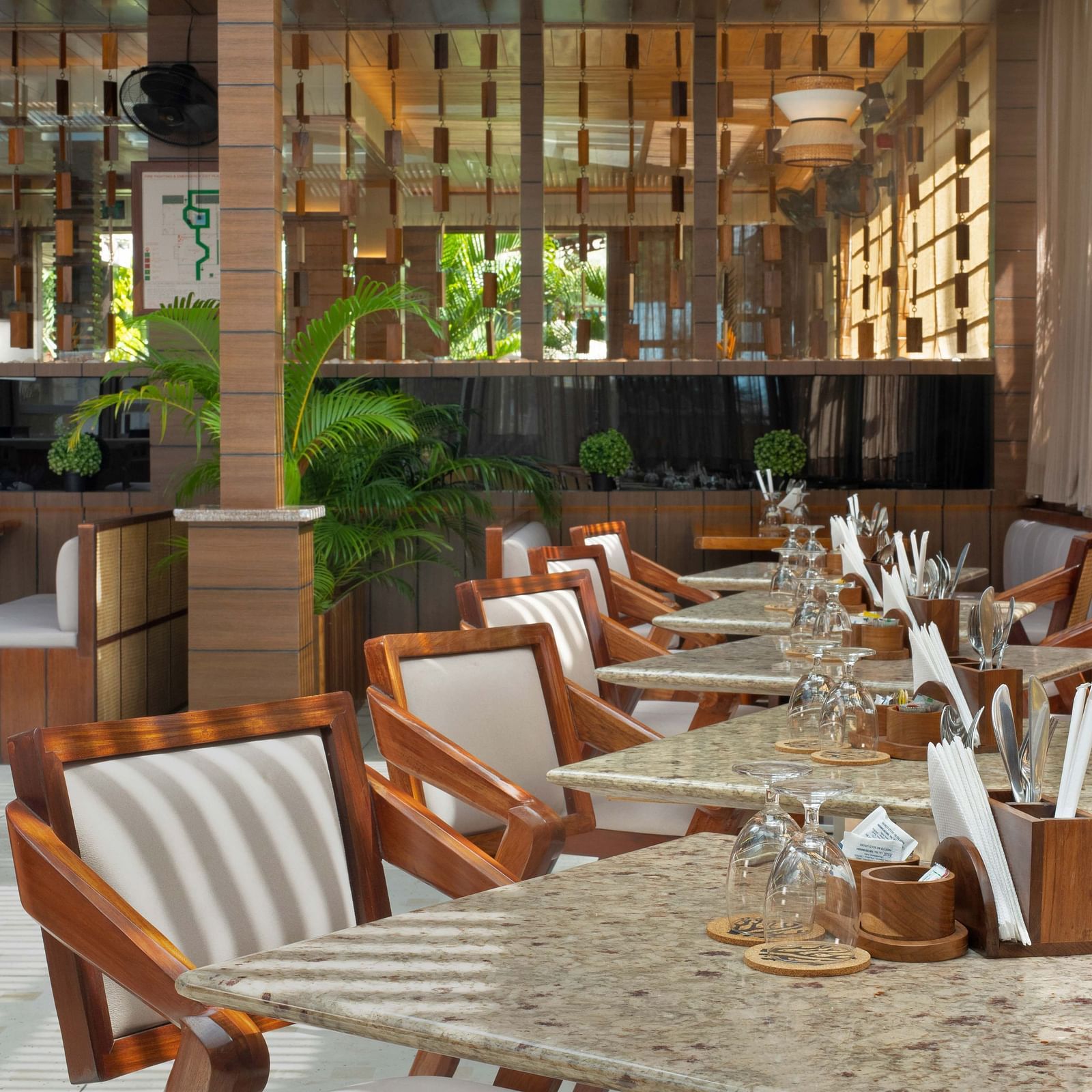 5th Bistro Cafe and Bar at Coral Reef Resort & Spa in Havelock featuring a dining area with outdoor seating, featuring wooden tables and striped chairs. The space is set in a lush garden with ample greenery, creating a comfortable, scenic setting - Coral R