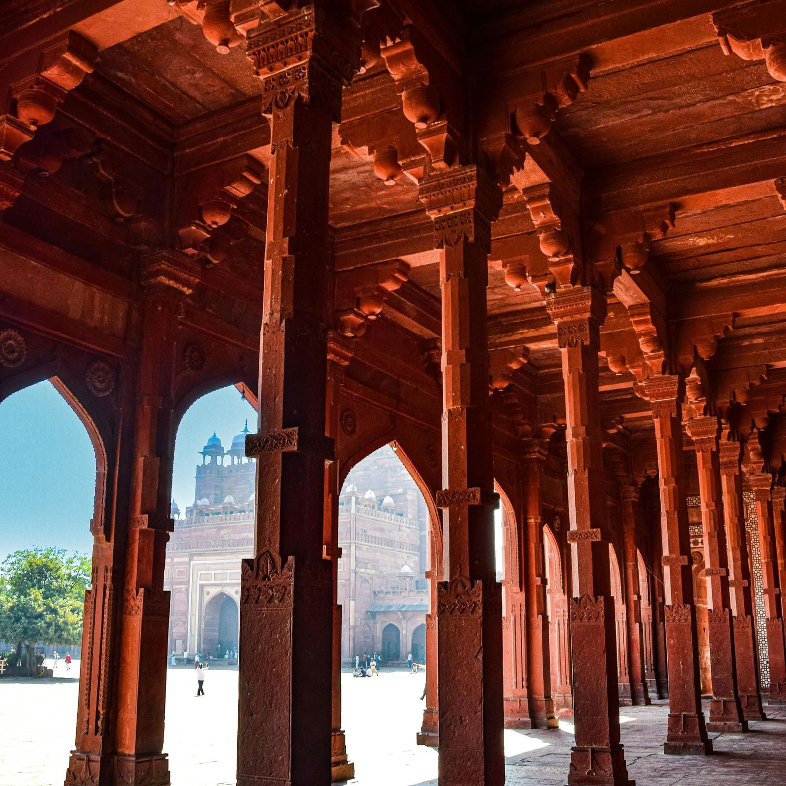 Covered corridor of a palace or temple with rows of carved pillars and arches, showing perspective depth.
