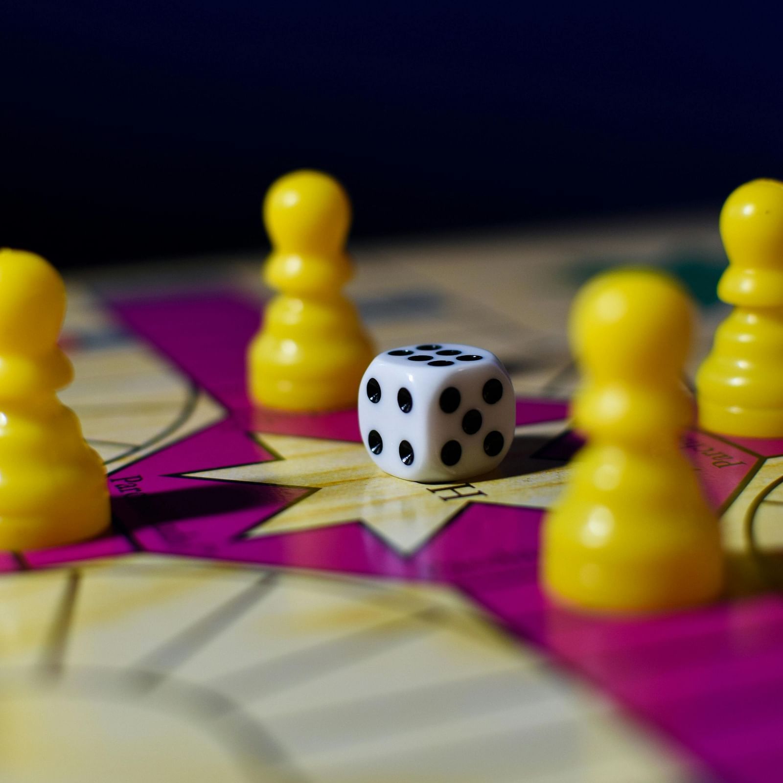 A board game with yellow playing pieces, a rolled dice, and a colorful game board.