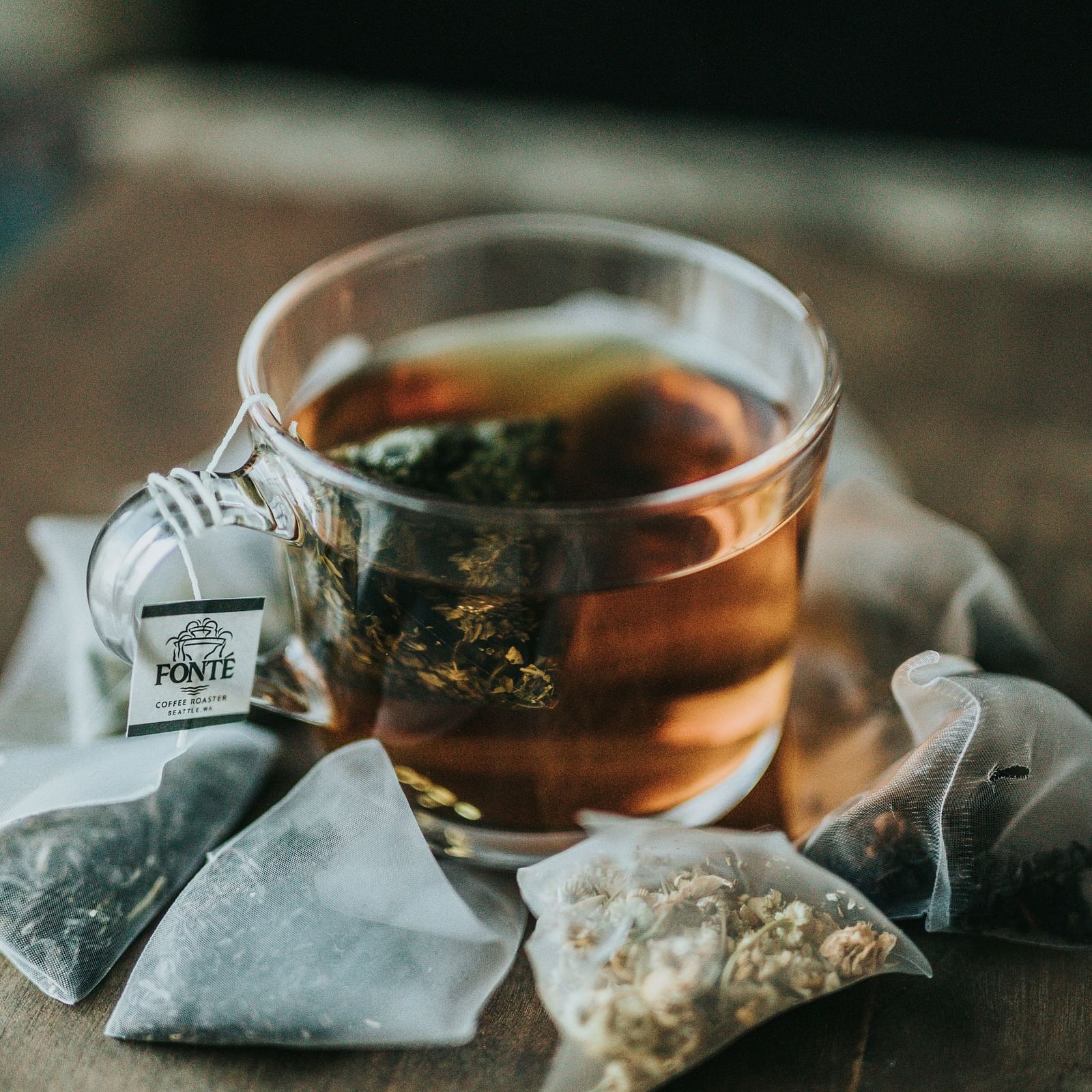 A clear teacup filled with amber-coloured tea alongside triangular tea bags