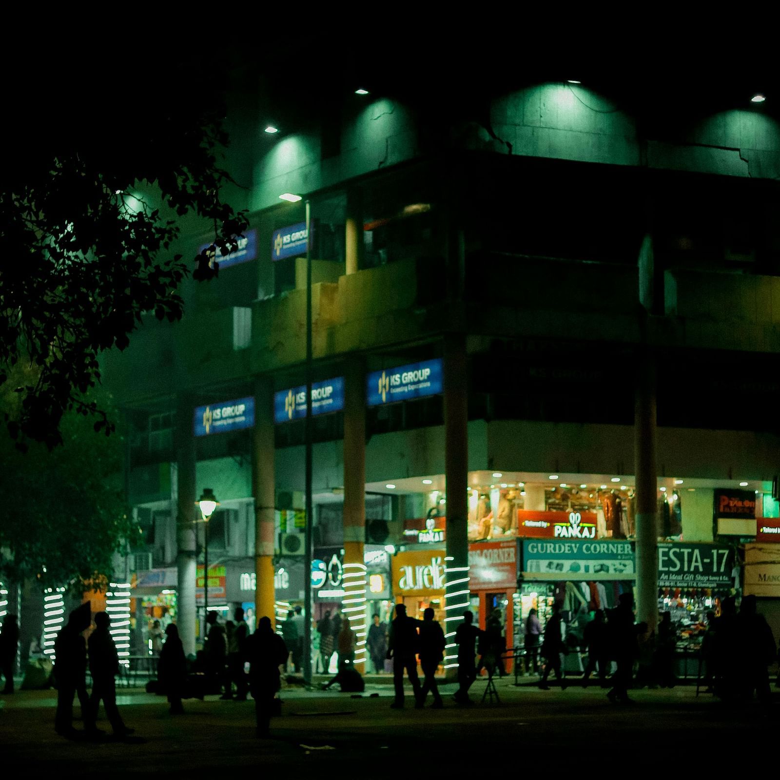 Facade of a shopping mall at night with people walking around in front of it.
