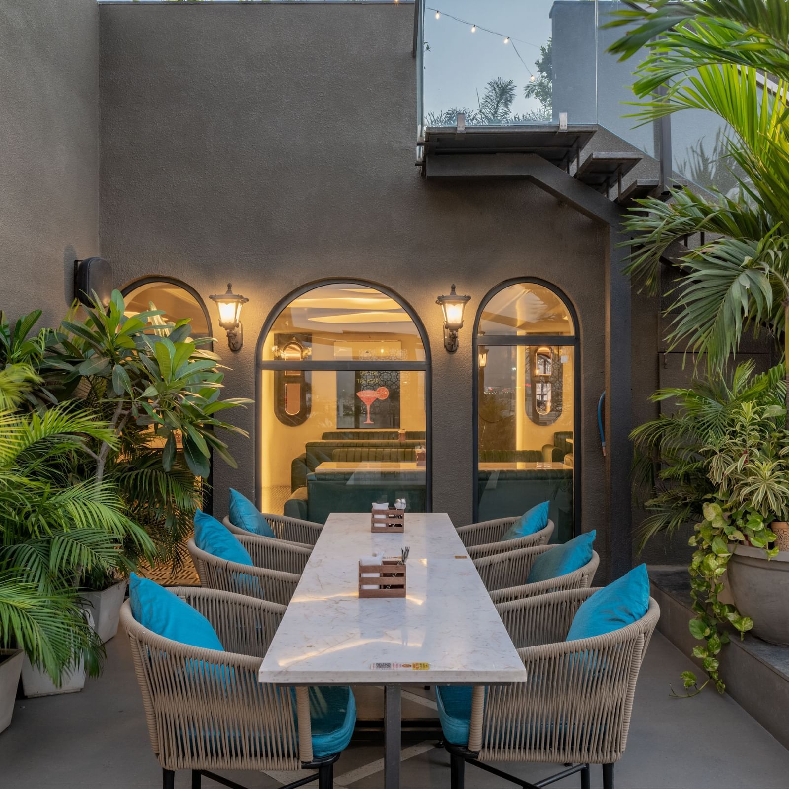Rooftop dining corner with wall lantern, arched windows, and planters at Hotel Highway King, Jaipur.