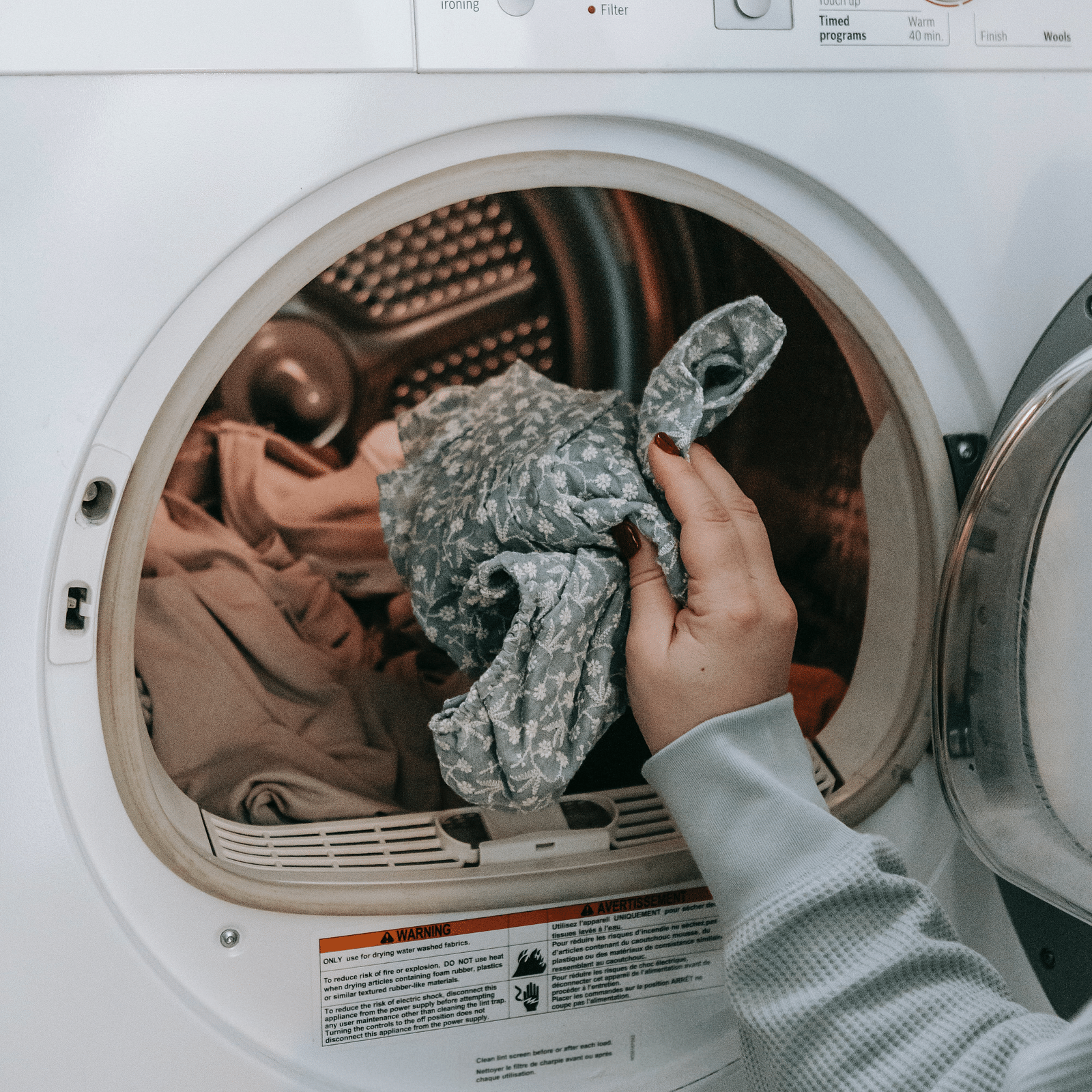 A person reaching into a front-loading dryer, removing laundry, with control panels visible above