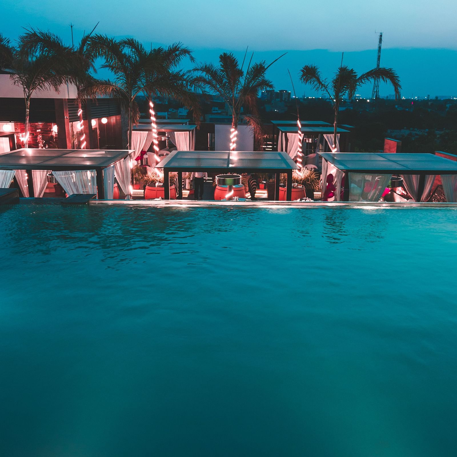 a view of a restaurant with an infinity pool beside and tents kept on the poolside - Hotel Park Elanza, Chennai