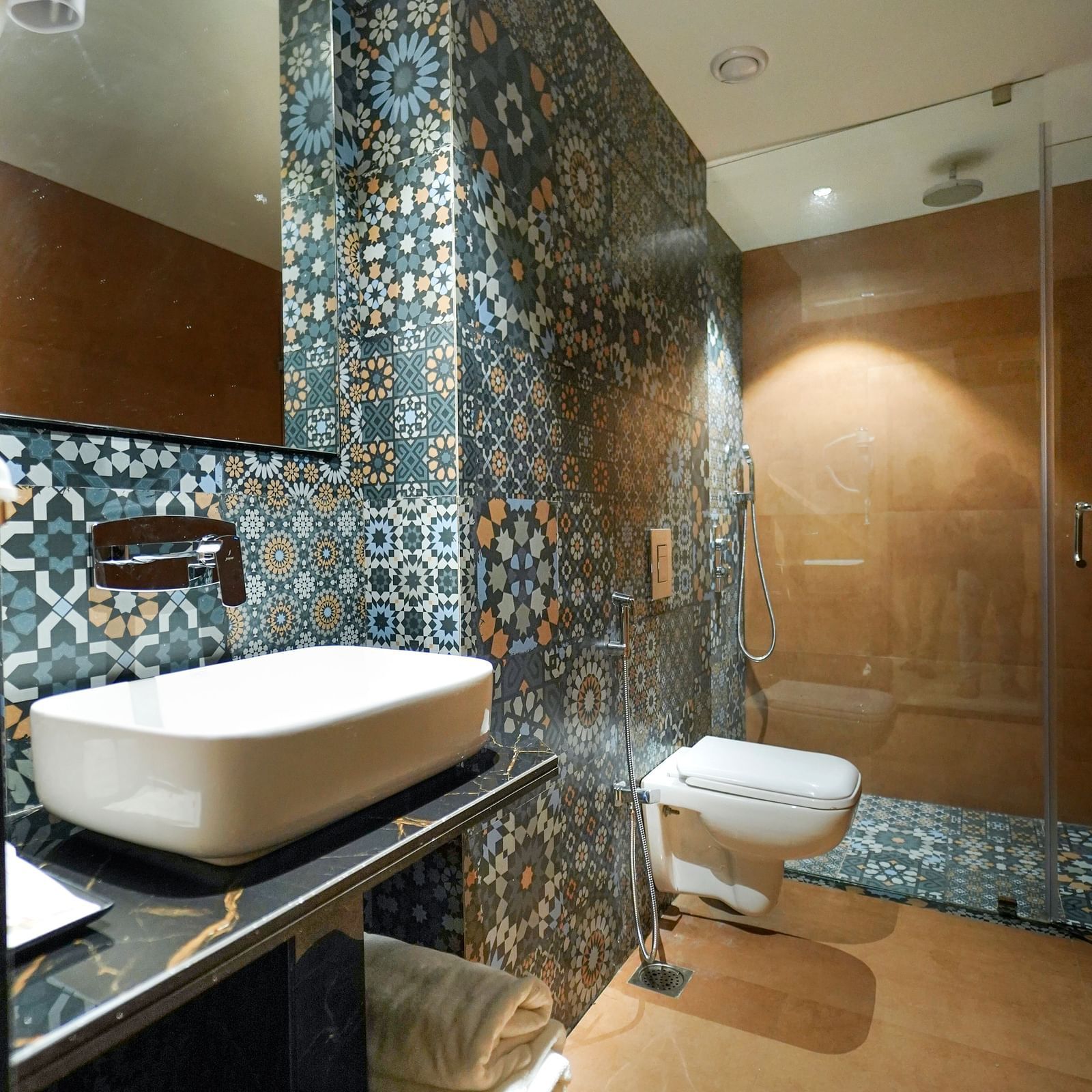 A modern bathroom features a freestanding bathtub, patterned tiles, a toilet, and a glass-enclosed shower area - Hotel Park Inn, Nellore.